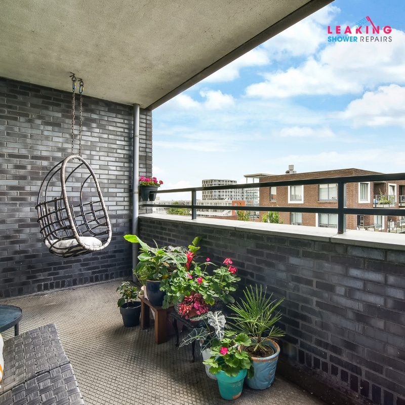 Cosy balcony with hanging chair, potted plants, and dark brick walls needing waterproofing.