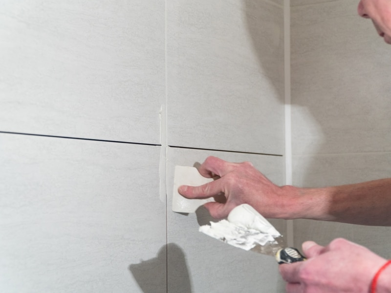 Close-up of a person applying grout to bathroom tiles to fix cracked grout between the tile joints.