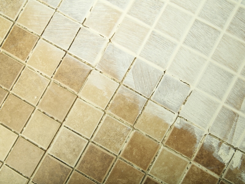 Close-up of tiled shower floor showing DIY shower leak repairs with white sealant.