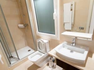 Modern bathroom with glass shower showing signs of potential shower base leaking under tiled floor.