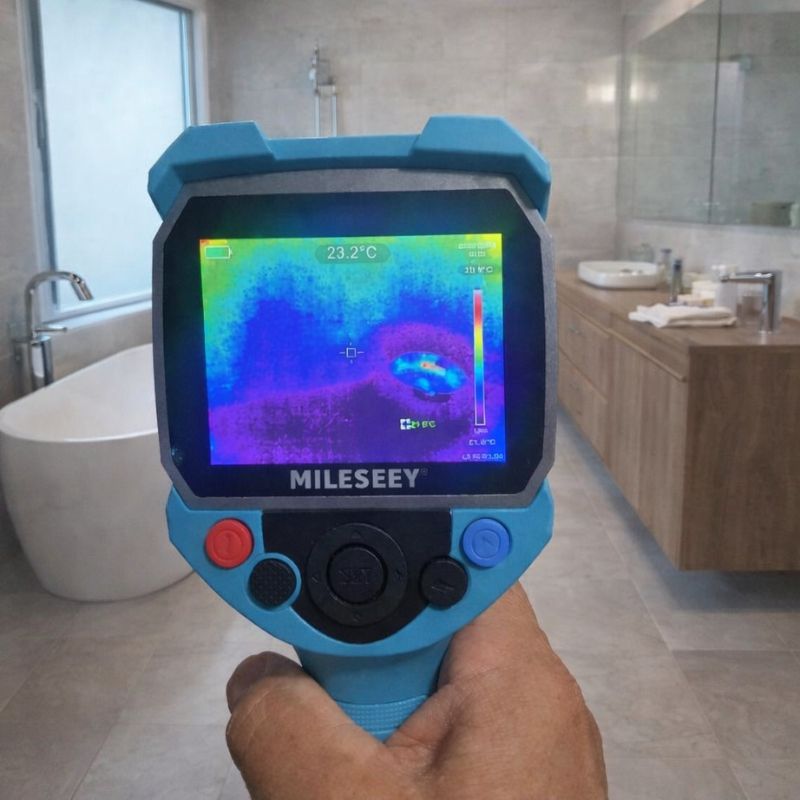 Handheld thermal camera scanning bathroom surfaces for hidden water leak source