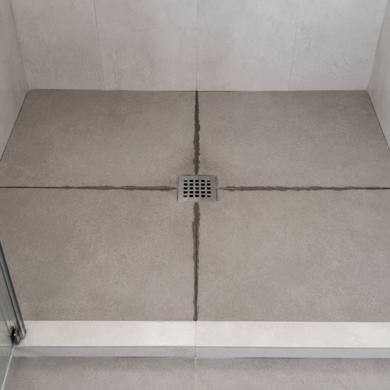 Shower floor tiles with grout lines that remain dark and damp while the surrounding tile is dry.