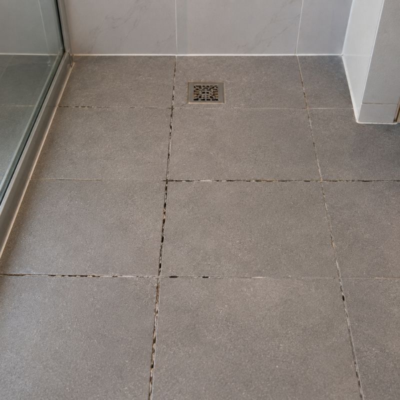 Ensuite shower floor before repair, with cracked and missing grout along several joints.