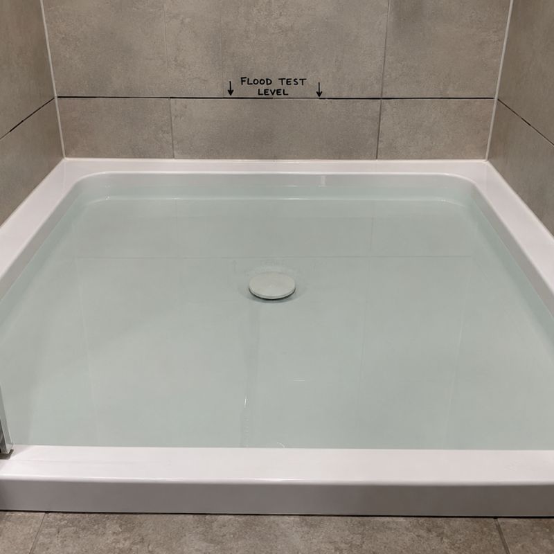 Shower base filled with water and the waste plugged during a timed flood test, with a level line marked on the tile