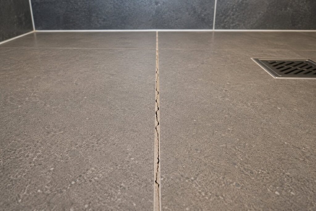 Hairline crack running the length of a grout joint in a shower floor, with the tile faces intact either side.