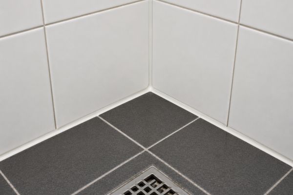 The same shower corner after repair, with refilled floor joints and a clean sealant bead at the base.